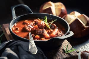 goulash soup served in black bowl with bread in background
