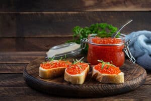 Delicious fresh red caviar with baguette toasts on wooden background